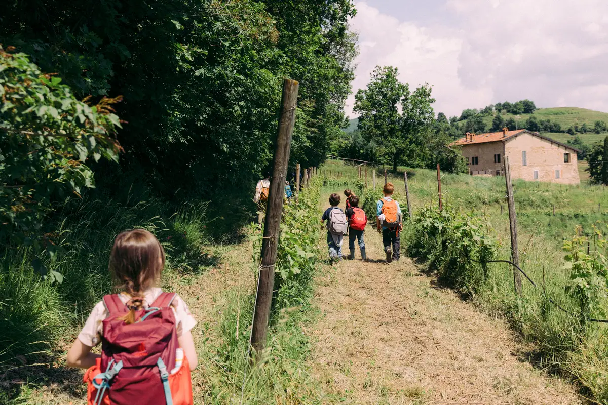 Bambini camminano lungo un sentiero tra alberi e prati