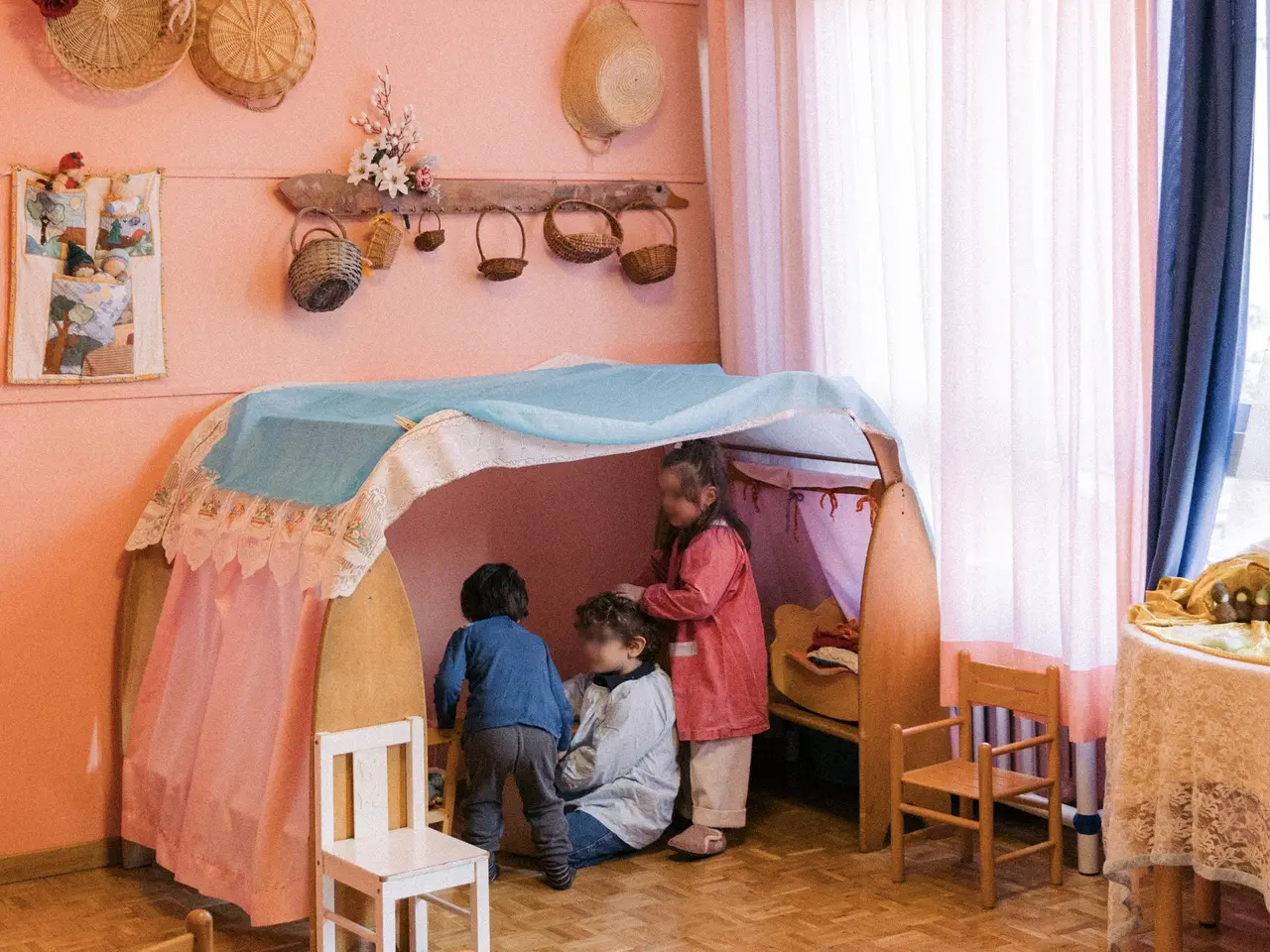 Bambini giocano in una casetta di legno nell’aula dalle pareti rosa