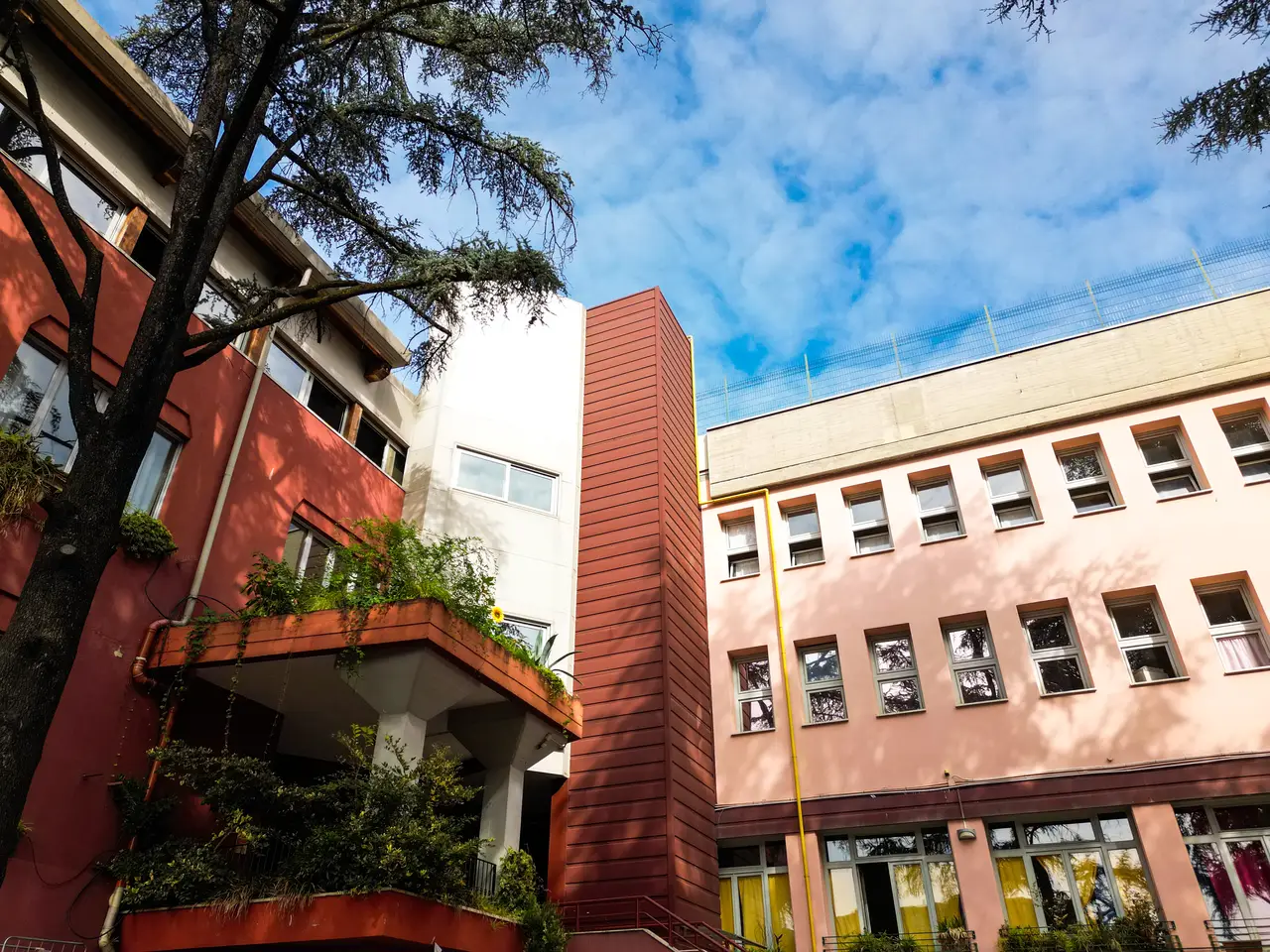La facciata della scuola di via Clericetti, tra alberi e cielo azzurro