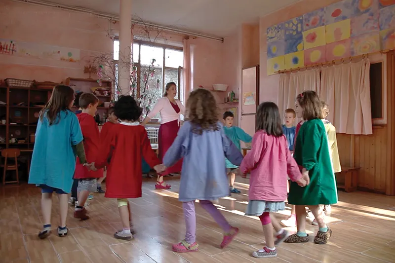 Bambini in grembiuli colorati fanno un girotondo in aula