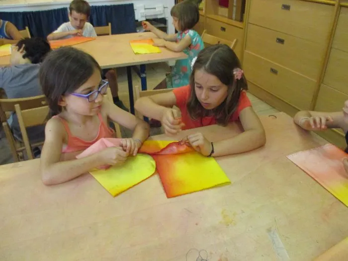 Due bambine dipingono ad acquerello su fogli gialli e arancioni